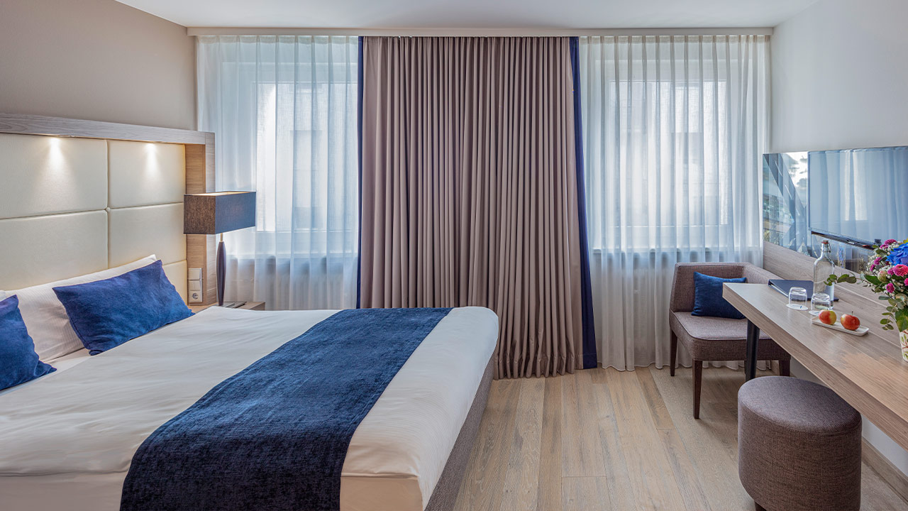 Helles Hotelzimmer mit Bett und blauer Tagesdecke