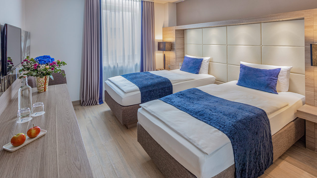 Helles Hotelzimmer mit Bett und blauer Tagesdecke