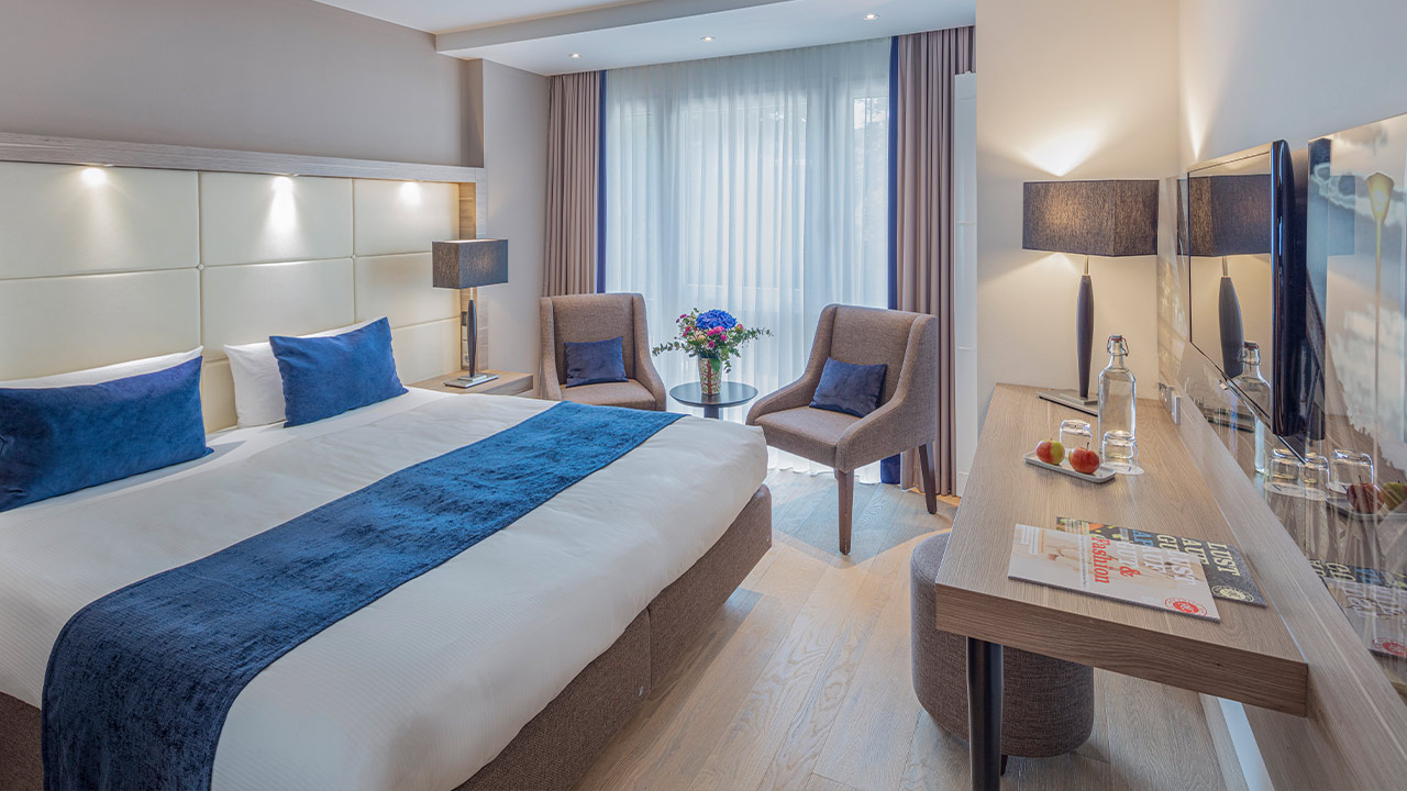 Helles Hotelzimmer mit Bett und blauer Tagesdecke