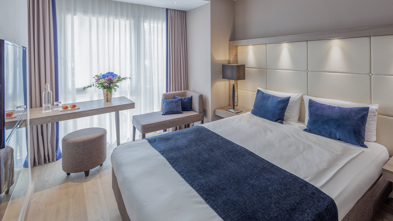 Helles Hotelzimmer mit Bett und blauer Tagesdecke