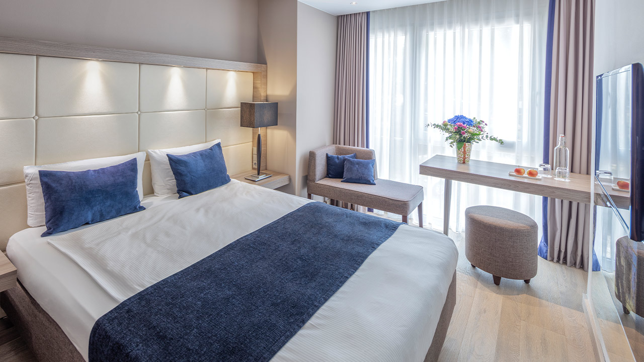 Helles Hotelzimmer mit Bett und blauer Tagesdecke