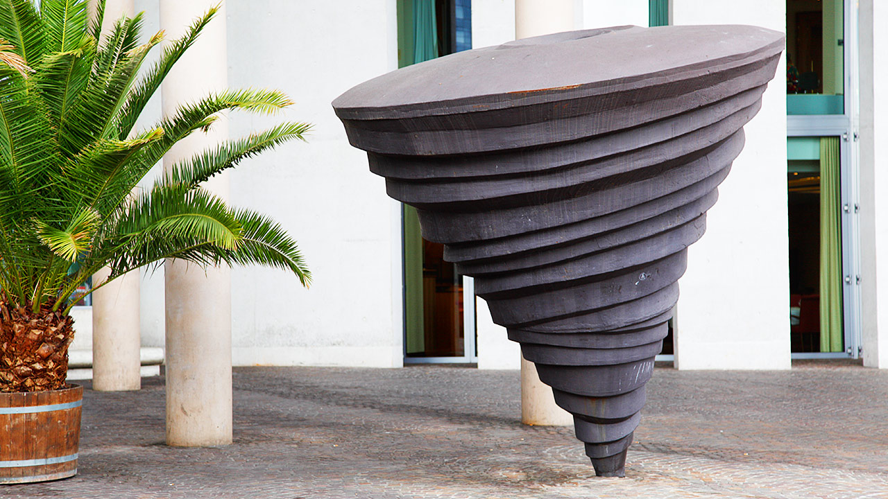 Künstlerische Skulptur, welche wie ein Wirbelsturm anmutet und Palmenpflanze daneben