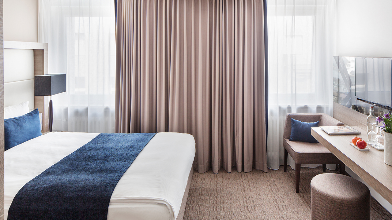 Helles Hotelzimmer mit Bett und blauer Tagesdecke