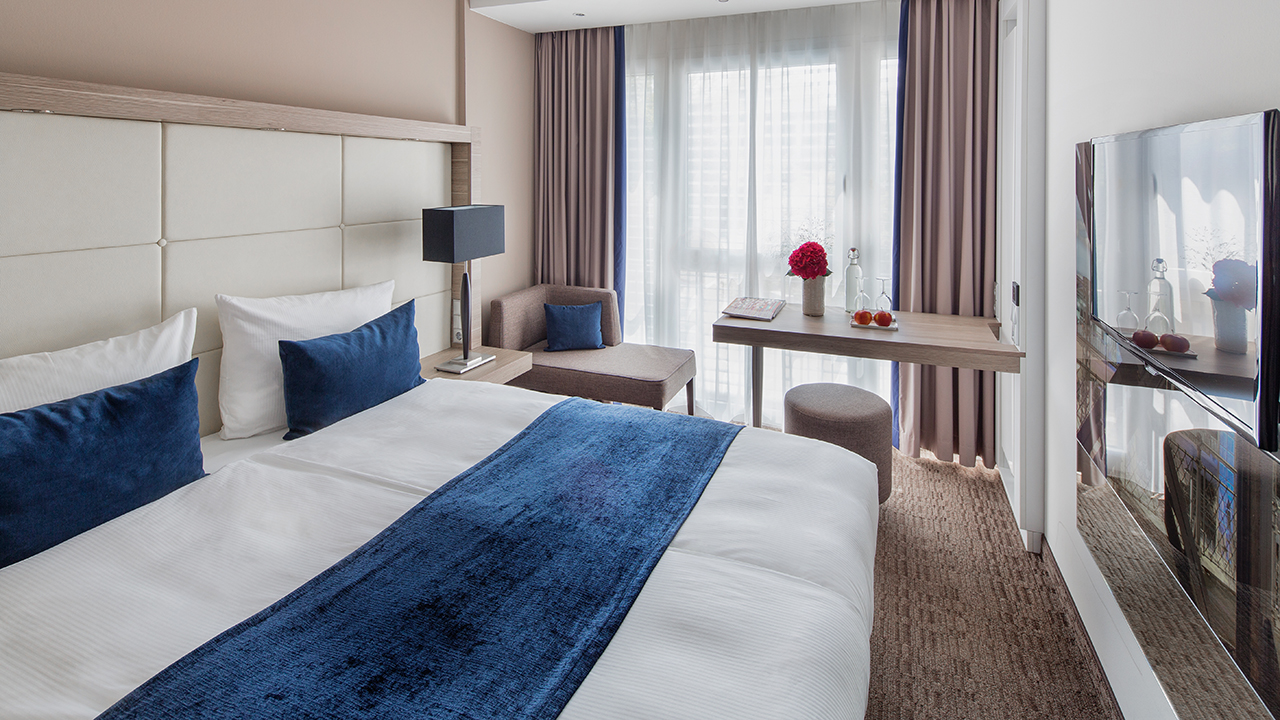 Helles Hotelzimmer mit Bett und blauer Tagesdecke