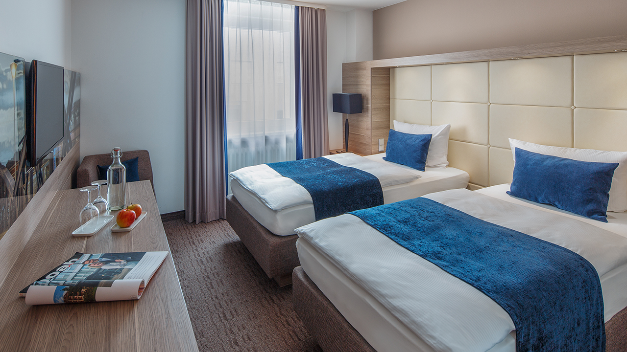 Helles Hotelzimmer mit Bett und blauer Tagesdecke