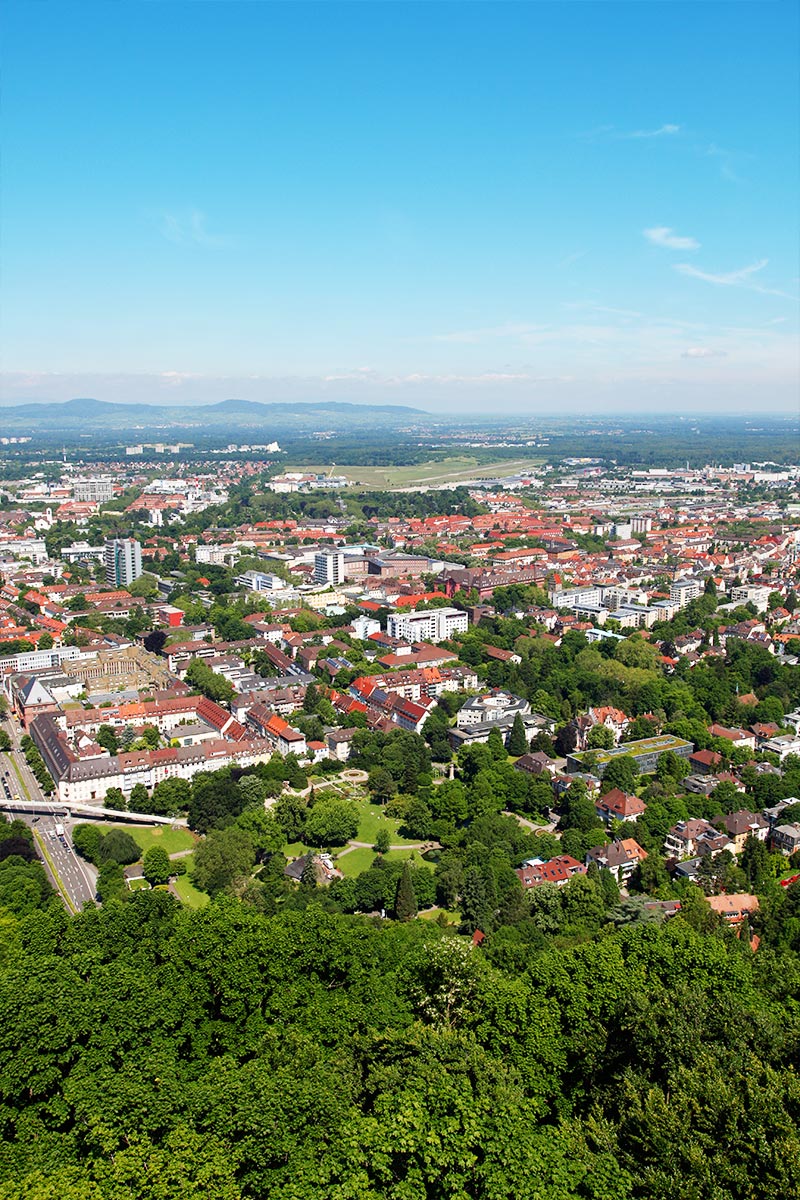 Luftaufnahme von Freiburg mit angrenzendem Waldstück vor blauem Himmel